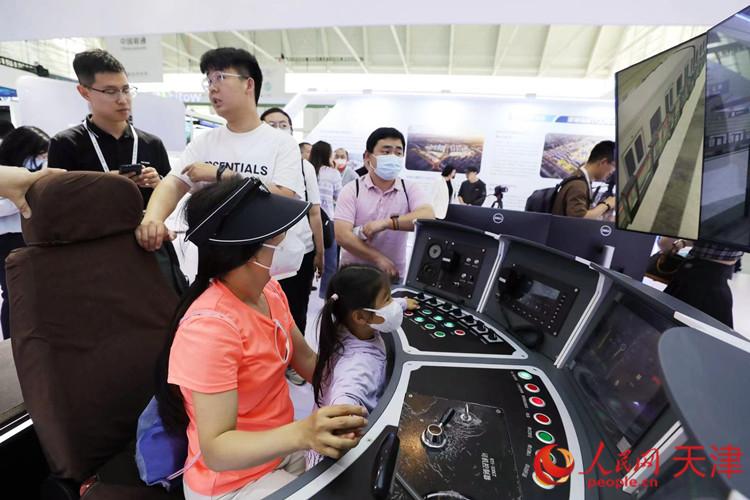 一位參觀者和孩子在天津軌道交通集團(tuán)展臺體驗智能駕駛帶來的樂趣。人民網(wǎng)記者 孫翼飛攝